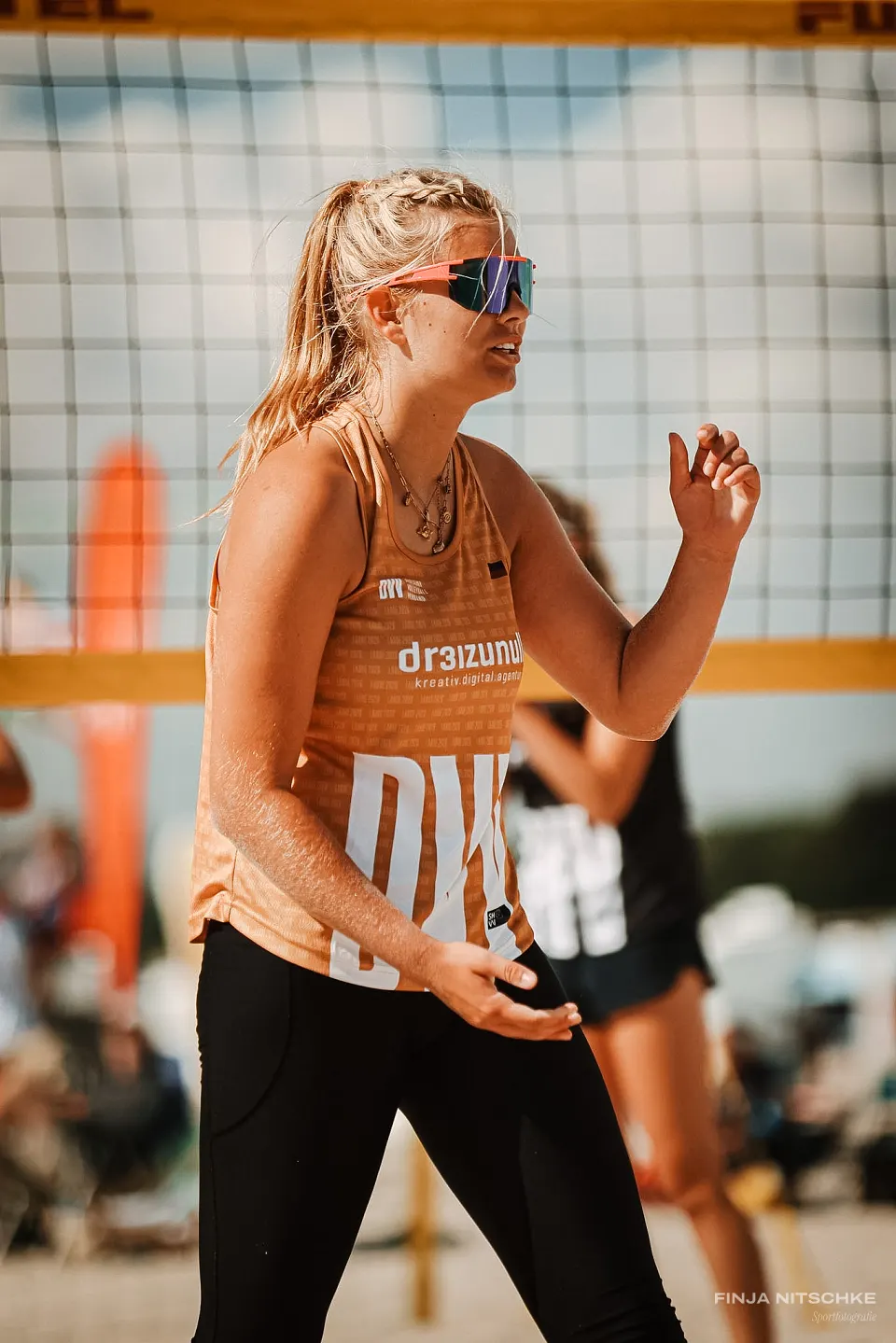 Konzentrierte Beachvolleyballerin mit verspiegelter Sportbrille vor dem Netz