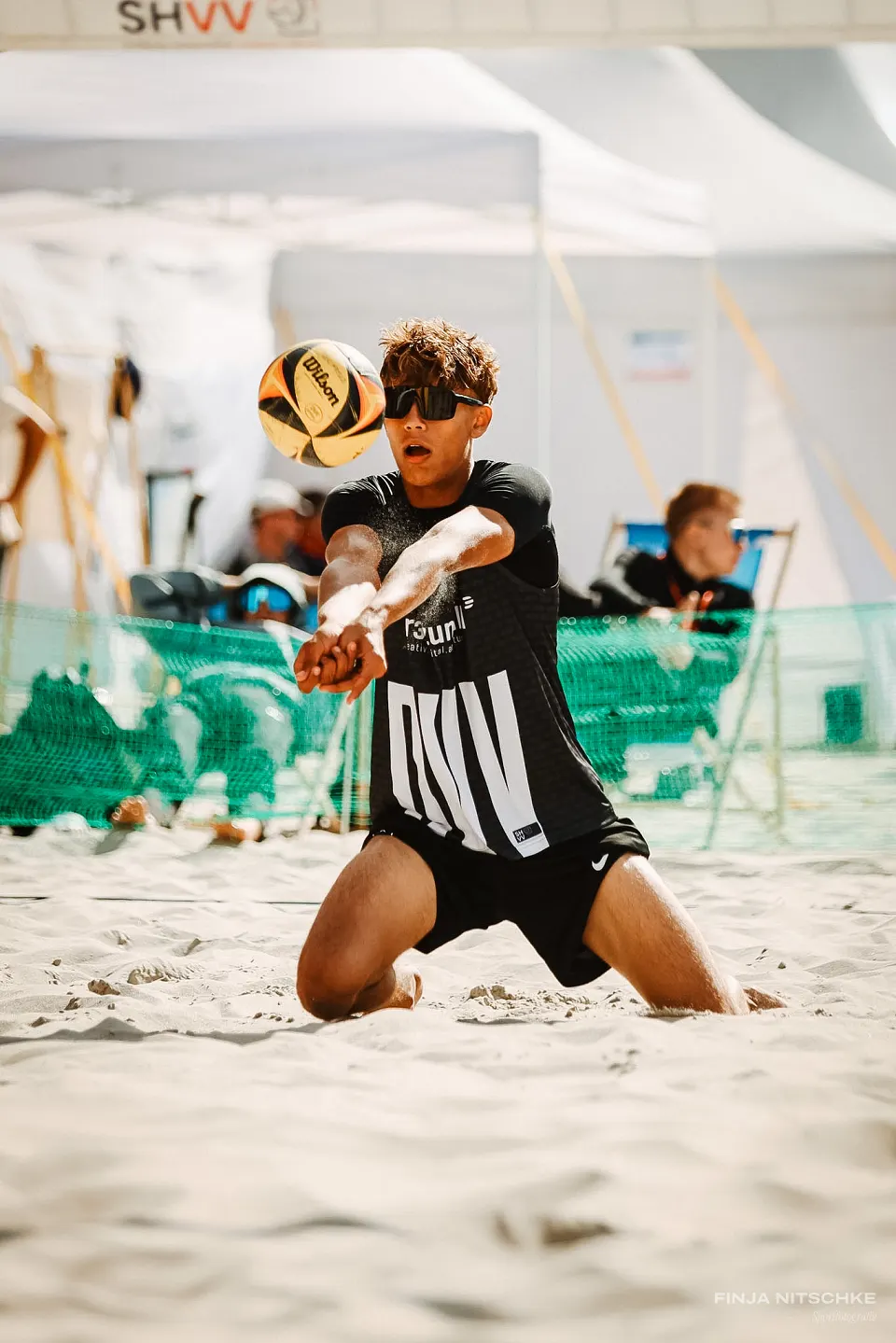Beach volleyball player digging the ball on his knees, sand dusting off his arms