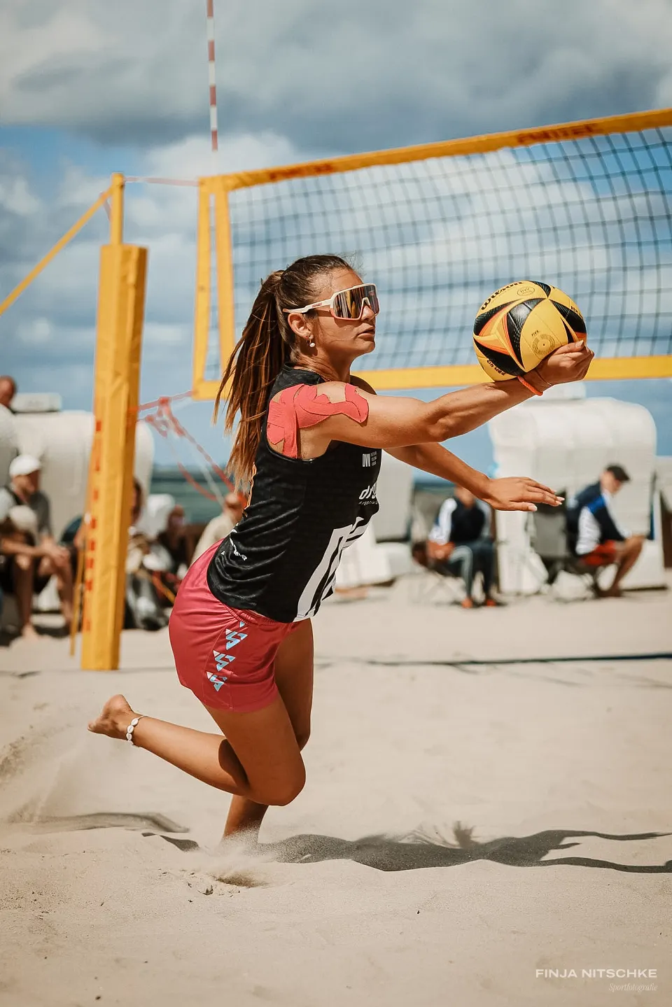 Beach volleyball player playing the ball in a lunge with an outstretched arm, sand flying